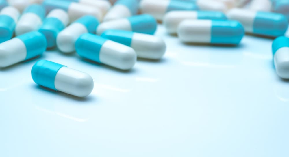 Selective focus on blue-white capsule pills. Capsule pills sperad on white background. Pharmaceutical industry. Pharmaceutics. Health and medicine concept. Pharmacy products. Drugs in hospital. Advanced technology collaboration to revolutionise pharmaceutical manufacturing