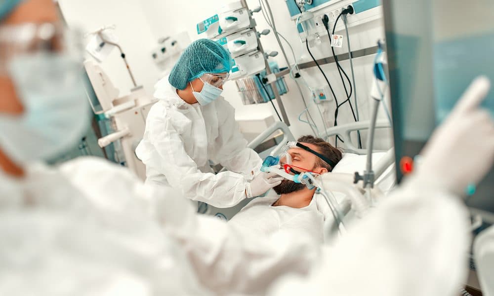 Doctors in protective suits put on a ventilation mask on a sick man with coronavirus disease covid-19, who is in an intensive care unit in a modern hospital. AI predicts global oxygen needs of COVID patients
